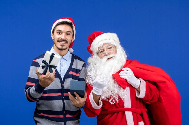 파란색 벽에 선물을 여는 젊은 남자와 산타 클로스의 전면 보기