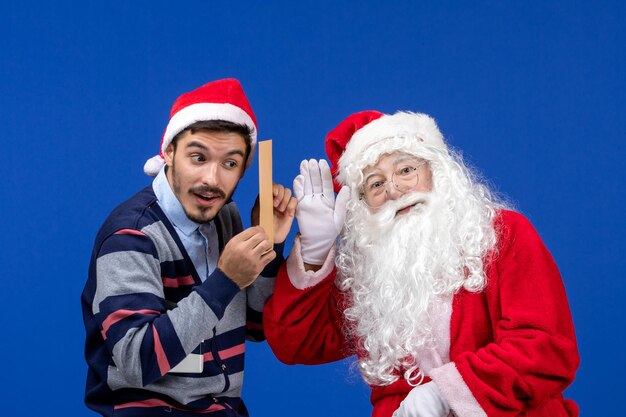 Front view of santa claus with young man whos holding letter on blue wall