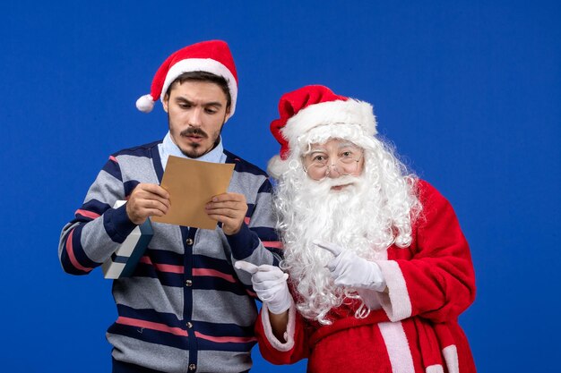 파란색 벽에 편지를 읽는 젊은 남자와 산타 클로스의 전면 보기