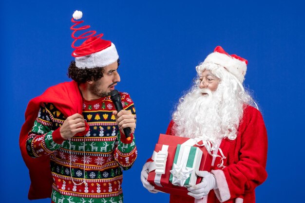 Front view of santa claus with young man whos using mic on blue wall