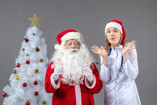 Front view of santa claus with young woman doctor on grey wall
