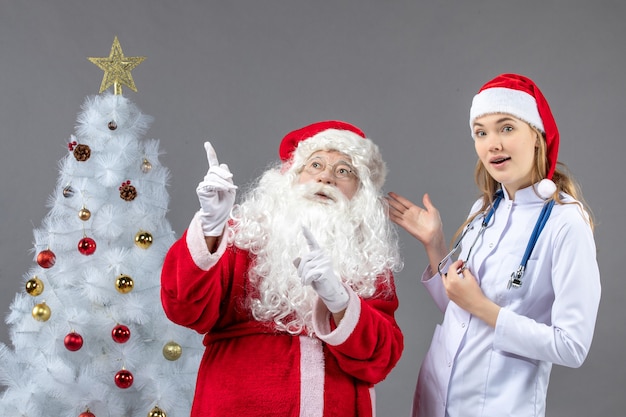 Foto gratuita vista frontale di babbo natale con giovane donna medico sul muro grigio