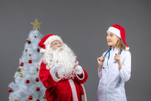 Front view of santa claus with young woman doctor on grey wall