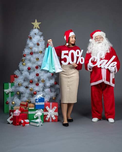 Front view santa claus with young woman holding and sale writings on gark rey background