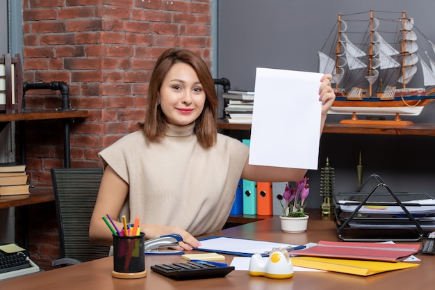 Front view of satisfied woman holding up documents sitting at wall