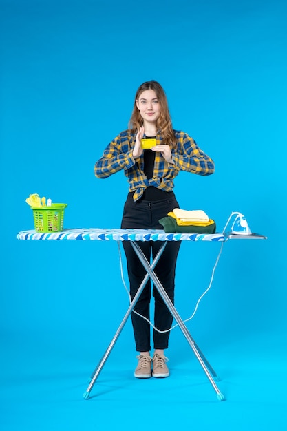 Free photo front view of satisfied young lady showing bank card and standing behind the ironing board in the laundry room