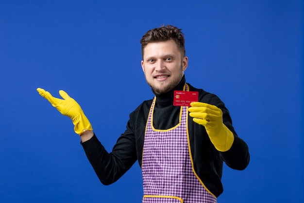 Front view of satisfied young man holding card on blue wall