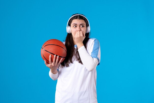 Front view scared young female with headphones holding basketball