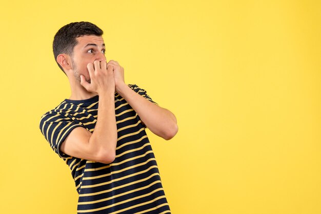 Front view scared young male in black and white striped t-shirt yellow isolated background