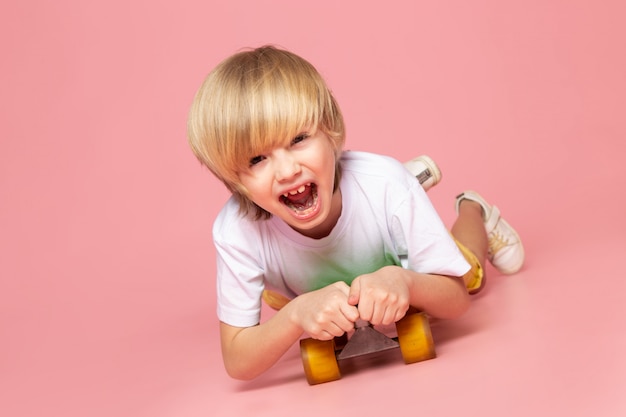 A front view screaming blonde boy riding green skateboard on the pink floor