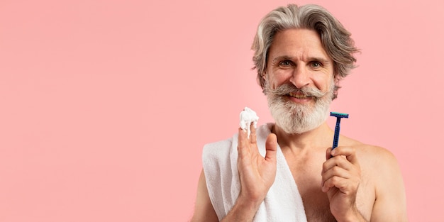 Front view of senior bearded man with shaving blade and copy space