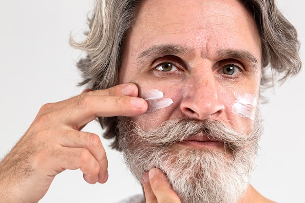 Free photo front view of senior man applying moisturizer