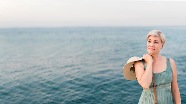 Front view of senior tourist woman posing next to ocean