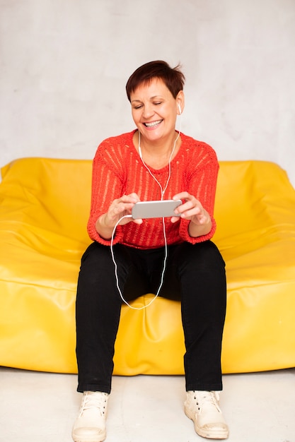 Free photo front view senior woman looking on phone and listening music