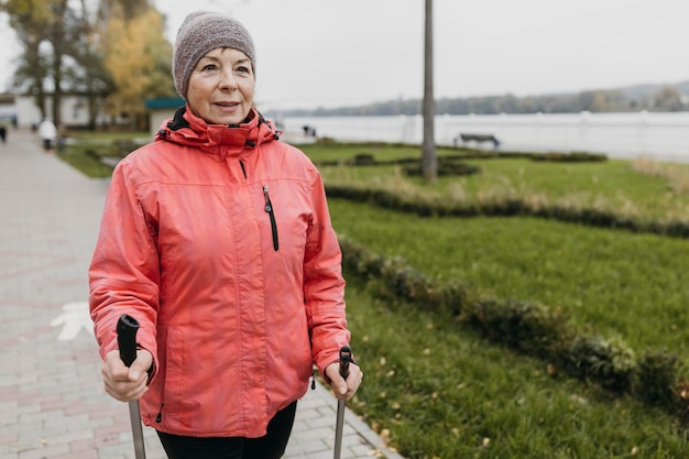 Foto gratuita vista frontale della donna senior all'aperto con bastoncini da trekking e copia spazio