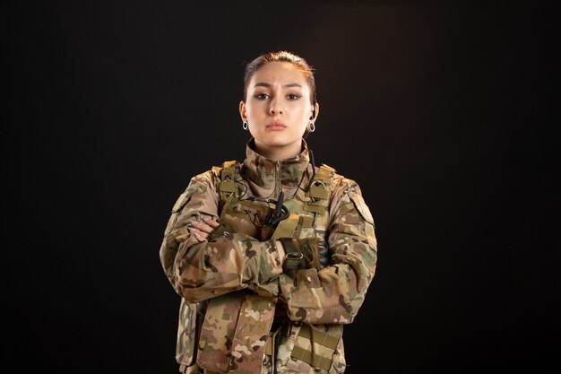 Вид спереди серьезной женщины-солдата в камуфляже на черной стене
