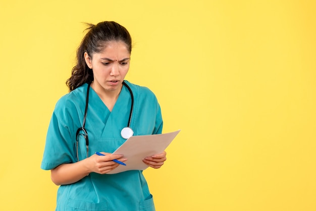 Вид спереди серьезная симпатичная женщина-врач, проверяющая документы на желтом фоне