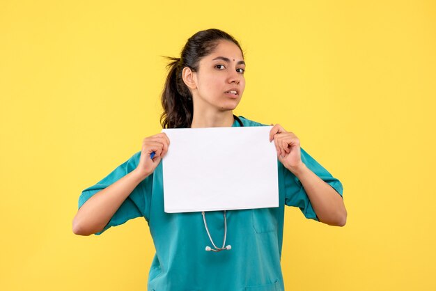 Front view serious pretty female doctor holding papers on yellow background