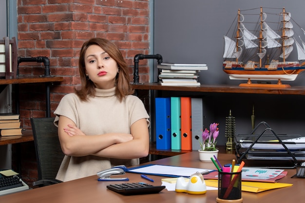 Vista frontale di una donna graziosa seria che incrocia le mani lavorando in ufficio