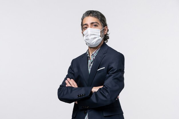 Front view of serious young guy in suit wearing mask on white surface
