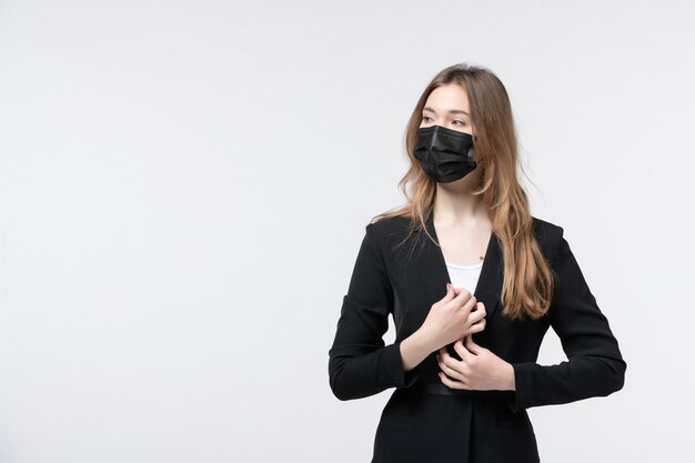 Front view of serious young lady in suit wearing surgical mask and looking at something on white