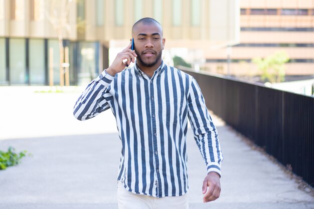 Front view of serious young man talking on phone during stroll