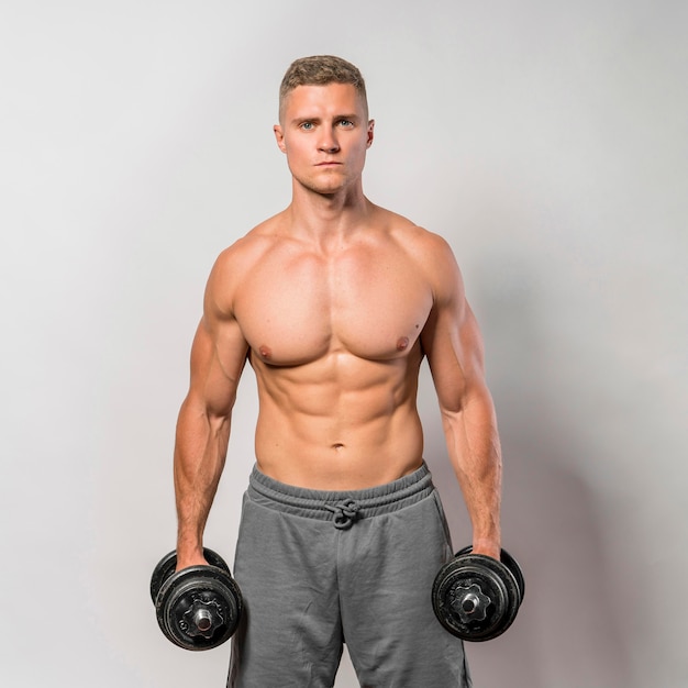 Front view of shirtless fit man posing while holding weights