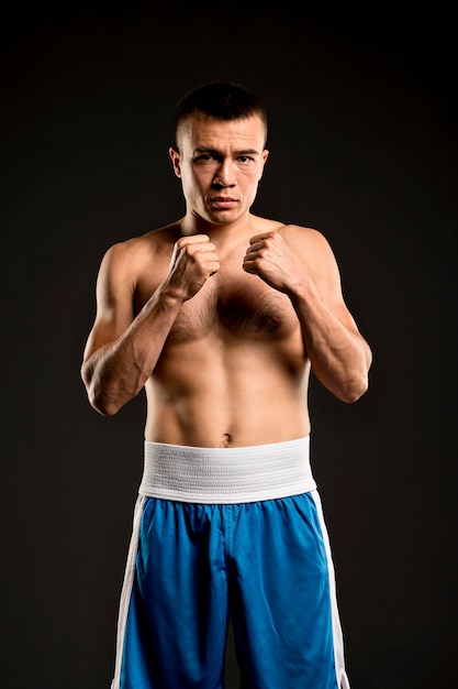 Front view of shirtless male boxer posing with fists ready