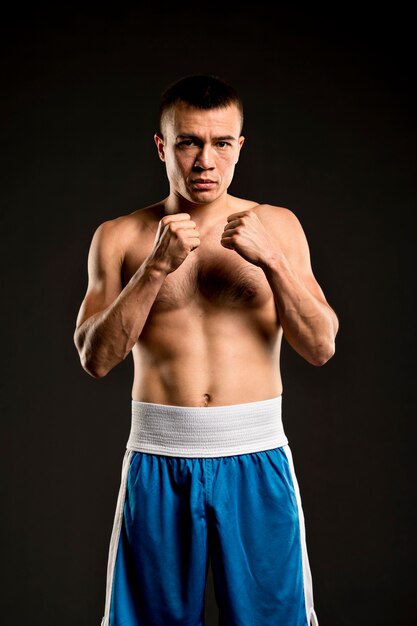 Front view of shirtless male boxer posing with fists ready