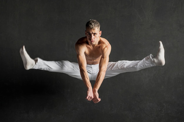 Front view of shirtless male dancer posing in mid-air