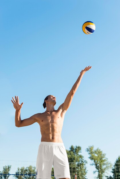 Front view of shirtless male volleyball player serving ball