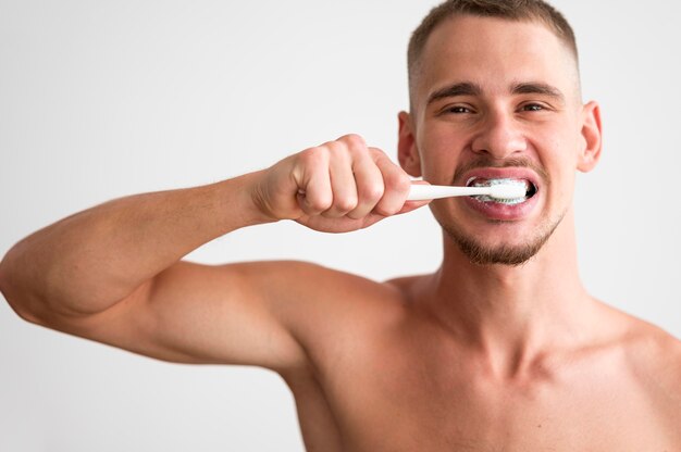 Front view of shirtless man brushing his teeth