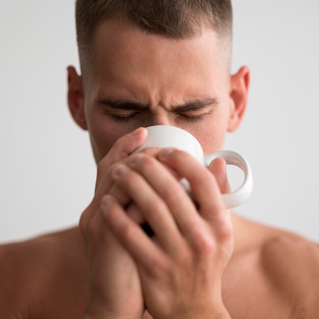 Front view of shirtless man drinking coffee in the morning
