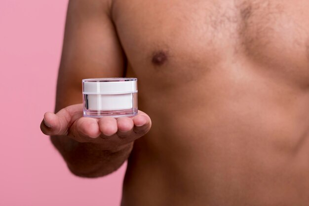 Front view of shirtless man holding face cream