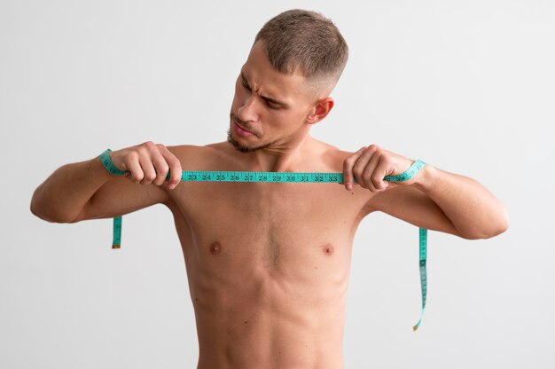 Front view of shirtless man holding measuring tape