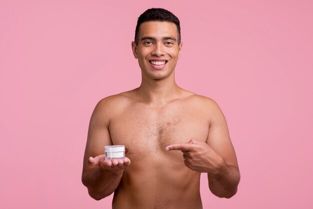 Front view of shirtless man holding and pointing at face cream