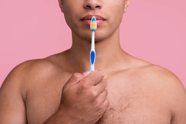 口の近くに歯ブラシを保持している上半身裸の男の正面図