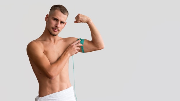 Front view of shirtless man measuring his bicep with tape