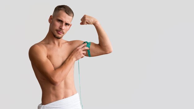 Вид спереди человека без рубашки, измеряющего бицепс с лентой