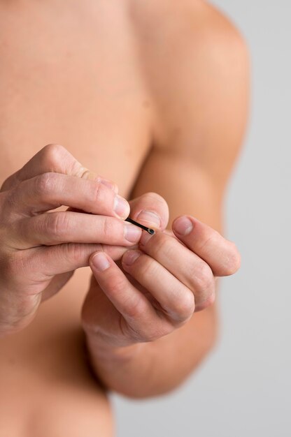 Front view of shirtless man taking care of his fingernails