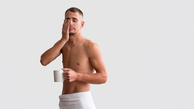 Front view of shirtless sleepy man in the morning with coffee