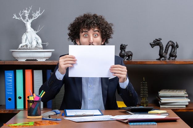 Free photo front view of shocked businessman holding up papers in front of his face in office