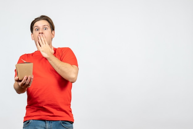 Вид спереди потрясенного эмоционального молодого парня в красной блузке, держащего коробочку на белом фоне
