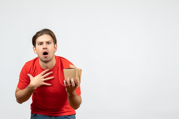 Front view of shocked young guy in red blouse holding small box on white background