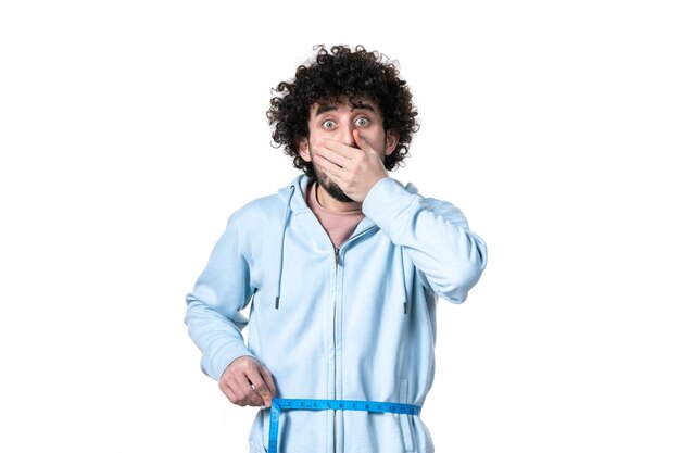 Front view shocked young man with measure tape on white