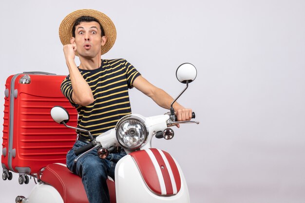 Front view shocked young man with straw hat on moped showing punch