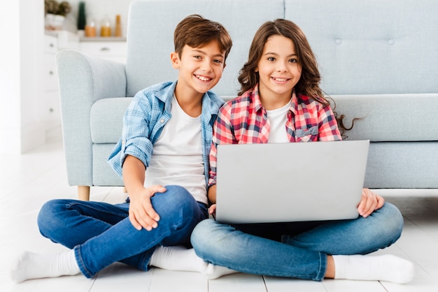 Front view siblings on floor using laptop