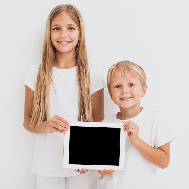 Free photo front view siblings holding a tablet mock-up