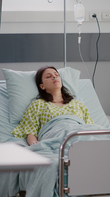 Front view of sick woman falling asleep recovering after cardiology recovery in hospital ward during medical therapy