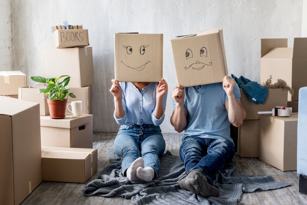 Front view of silly couple with boxes over heads at home on moving day